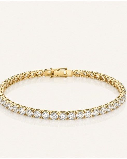 Gold-coloured tennis bracelet of round clear stones in prong settings, lying on burgundy velvet with three other tennis bracelets.